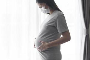 Young pregnant woman wearing a protective mask and expecting a baby, healthy and motherhood concept photo
