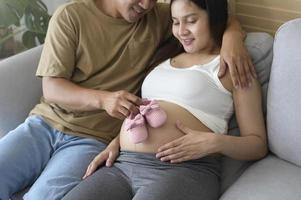 Young pregnant woman putting baby shoes on tummy, family and pregnancy care concept photo