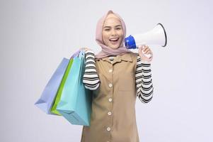 Young beautiful muslim woman in suit holding colorful shopping bags over white background studio photo