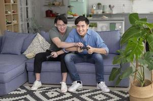 Young smiling gay couple playing video games in the living room at home, LGBTQ and diversity photo