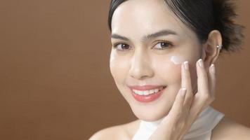 una mujer joven con una cara hermosa está sosteniendo crema, usando crema de su cara, concepto de belleza para el cuidado de la piel foto