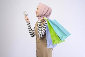 Young beautiful muslim woman in suit holding colorful shopping bags over white background studio photo