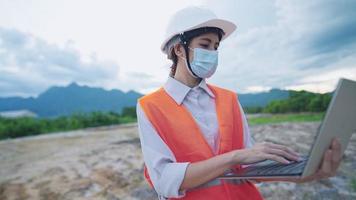 Young female engineer wear safety vest protection and helmet working with portable laptop at outdoor construction land site, specialist expert job, structure planning analysis design, hard worker video