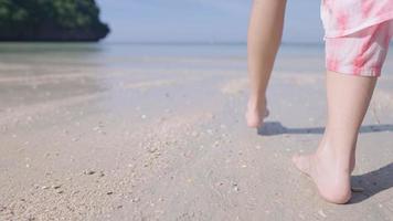 kvinna barfota som går på öns strand, små lugna vågor som lämnar fotspår på sanden. varmt soligt väder, klart havsvatten, frihetsliv flykt från staden, sommarsemester i thailand video