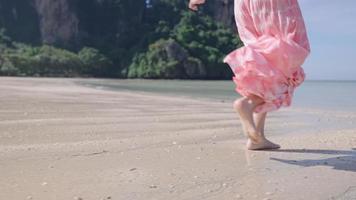 onderlichaamsdeel vrouwtjes in roze strandkleding lopen in de oceaan op het strand van het tropische eiland, zeewater spatten in slow motion. zomervakantie reisbestemming paradijs op aarde leuk en vrolijk video
