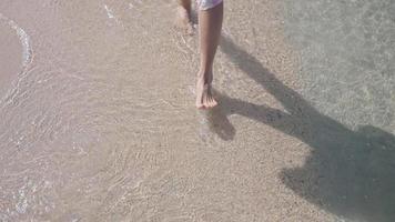 top view female barefoot walking on the sand beach, sea waves and crystal clear water. Hot sunny weather, tropical island beach, summer vacation travel destinations, relaxing walk on calm beach video