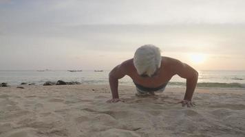 Strong active senior white hair man doing bodyweight pushups on the beach, remote workout on the island, outdoor exercises self motivation, morning exercise, get away from crowed city, refresh energy video