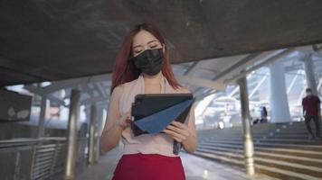 linda mulher trabalhadora asiática andando na passagem metropolitana a pé segurando tablet e papel de trabalho, telecomunicações de tarde ocupada, senhora independente trabalha no centro da cidade, usando aparelhos digitais video