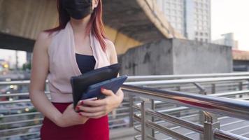 Confident asian young working woman walking on the elevated overpass showing modern urban lifestyle wear medical face mask when going outside, diseases risk prevention, young entrepreneur asian lady video