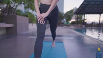 bild framifrån av ung kvinna som sträcker ut sina ben stående på träningsmatta på offentliga rekreationscenter utomhuszon, vältränade och fasta sätesben, hälsosam flexibel balanserad kropp, utomhusträningsposter video