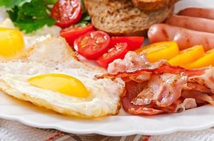 English breakfast - fried eggs, bacon, sausages and toasted rye bread photo