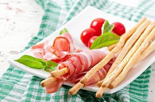 Grissini bread sticks with ham, tomato and basil photo