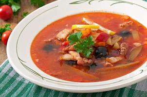 Soup solyanka Russian with meat, olives and gherkins in wooden bowl photo