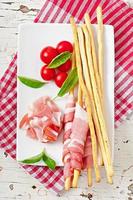 Grissini bread sticks with ham, tomato and basil photo