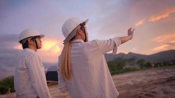 ingeniero y arquitecto discutiendo sobre el proyecto de construcción de edificios en terrenos llanos al aire libre durante la puesta de sol, experiencia especializada trabajando horas extras hasta tarde, innovación en inversión inmobiliaria video