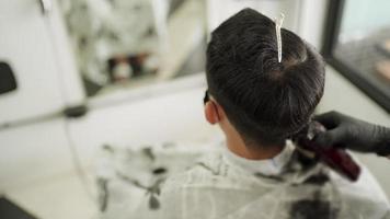 ci-dessus tourné à l'intérieur du salon de coiffure, un homme asiatique porte un masque de protection se fait couper les cheveux. bien toilettage, tondeuse à cheveux électrique, barbier pendant le virus corona covid-19 réouverture des affaires après la pandémie, vue de dessus