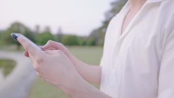 close-up op witte huid mannelijke handen typen op telefoonscherm terwijl rusten in natuurpark, ontspannende oefening, recreatieve activiteit buiten, draagbare informatietechnologie, communicatieapparaat op afstand video