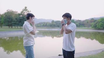 Friends put on protective medical face mask in park to protect each other health to avoid spread of coronavirus or covid-19, social distancing, stop spreading of body secretion due to pandemic. video