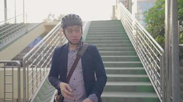 close-up in cirkel bekijk een fietsliefhebber of actieve zakenman die zijn fietshelm verwijdert en geniet van een natuurlijk uitzicht op het groene viaduct in het midden van de stad, terwijl hij vrolijk naar huis loopt, video