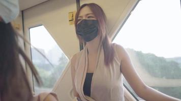 jonge mooie aziatische vrouw in zakelijke kleding draagt een zwart gezichtsmasker dat in de metro staat, veilig reizen met het openbaar vervoer, twee vrouwen die een gesprek hebben in de skytrain video