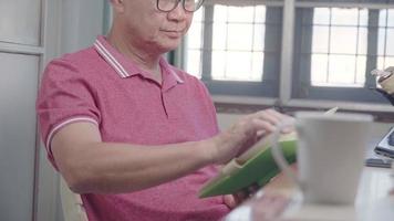 Old man asian professional golfer reading alone green old book at home, old aged lifestyle, home leisure hobby and people concept, senior retiree man sitting at table relaxing chilling on weekend video