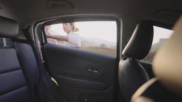 Young helpful dyed blonde daughters opening a car door for her mother to sit in, an elderly caregiver getting ready for older by fasten a back belt and close door, older people homecare concept video