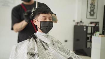 jovem asiático usando máscara facial protetora enquanto corta o cabelo, prevenção de doenças infecciosas, novo estilo de vida normal. pandemia covid-19 reabrir negócios. video