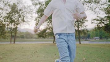 homem não reconhecido correndo despreocupado com os braços estendidos em um parque verde de verão, máscara facial no bolso da calça jeans, vida normal após a epidemia de covid-19, luzes do sol brilham no topo das árvores à vista video