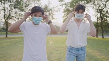 jovens amigos asiáticos colocam máscara facial protetora protegendo-se do vírus de doenças infecciosas transmitidas, jovens adultos usam máscara facial médica em pé dentro do parque novo distanciamento normal