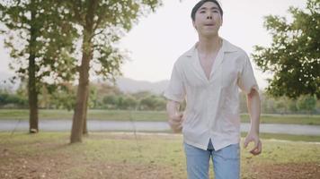 Young man running in the park during sunset, showing relaxing and relieved positive emotion, escape from the city, human and nature, light skin male wear short sleeves shirt and Jeans, slow motion video