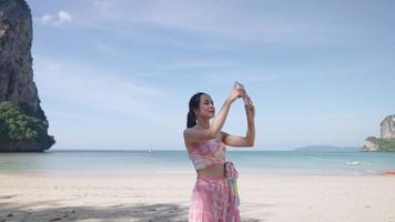 Young beautiful asian woman video calling via phone internet while travels on vacation, using video recording to collect memories, natural asia resources, a barefoot relaxing walking on beach activity
