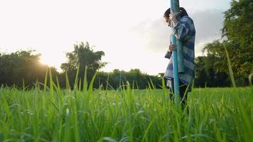 Young asian country girl holding blue pvc pipe going on the crop grass field get ready for work inside organic farm , sustainable agriculture, diy working equipment, simple domestic asian life video