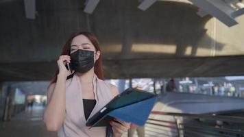 joven y atractiva mujer asiática vestida de negocios de moda caminando hablando por teléfono en un puente peatonal, secretaria multitarea lee en una tableta digital, un entorno empresarial de la ciudad video