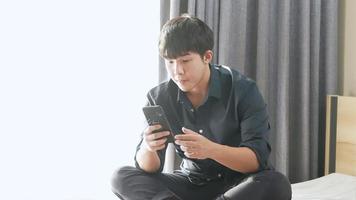 Asian IT person texting an online message using application on mobile phone while sitting on comfortable at home, business man using phone browsing on live financial stock market, home entertainment