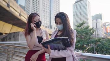 Two young adult working age female friends wear business attire outfit having fun with their conversation standing outdoors surrounding by high rise building, city downtown vibe, urban lifestyle video