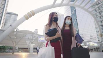 Asian female colleagues walking to work together, carrying office bags and stuffs with downtown business area, modern city life, stock trading consultant, employee adpt with new normal lifestyle video