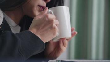 närbild asiatisk kvinna som dricker varm dryck från kaffemugg, håller i vit kaffekopp, varmt te på avkopplande tid hemma, hälsosam livsstil, bär tröja enkelt hemliv, sidovy, håll dig varm video