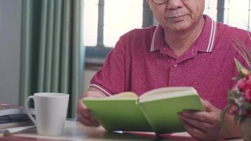 homem asiático de meia idade abre a página do livro revisando a sabedoria do conhecimento na mesa de trabalho em casa, educação nunca é tarde demais, educação à distância, curso de estudo remoto para idosos, foco masculino sênior e concentração video