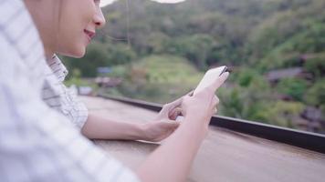 gelukkige jonge vrouw in casual stijl die plezier heeft met sms'en op mobiele telefoon en glimlachen, prachtig natuurlijk landschap op de achtergrond, technologie draadloos overal, reisvakantie buiten de stad concept video