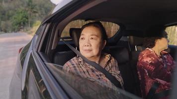 Elderly looks out of car window to enjoy a rural side way view while sitting in the back seat next to other family member, sunlight on face, safety through out the road, family in car, freedom of life video