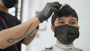 salon de coiffure masculin asiatique, l'homme porte un masque noir se fait couper les cheveux. opportunité d'emploi barbier. pulvérisation et peignage des cheveux, industrie du barbier pendant la réouverture du virus corona covid-19 après la pandémie, ralenti video