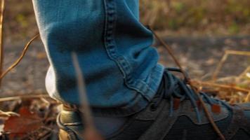 Männerfüße in Jeans und Turnschuhen treten auf trockenes Gras, das mit Stöcken und gelben Laub auf Waldwegen übersät ist extreme Nahaufnahme Zeitlupe