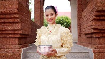 tiro portátil, retrato de mulher bonita no festival songkran com traje tradicional tailandês no templo segurando a tigela de água e sorriso. cultura da tailândia com festival de água video