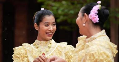 handheld shot, selectieve focus, jonge mooie vrouwen met thais traditioneel kostuum genieten van opspattend water in de tempel op songkran festival. thais nieuwjaar, thailandcultuur met waterfestival video