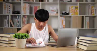 retrato de homem asiático cansado em singlet usando laptop e procurando documento em casa. homem sonolento trabalhando em casa, pensando e se sentindo pensativo. trabalhando em casa com sobrecarga à noite no novo normal. video