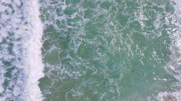 zoom uit bovenaanzicht van zeegolven die op de rotsen van de kust neerstorten en een explosie van water creëren. prachtig tropisch strand. geweldige zandige kustlijn met witte zeegolven. natuur, zeegezicht en zomer. video