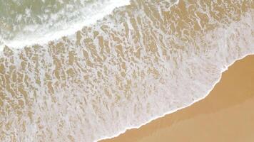 vista aérea de la playa de arena y la textura de la superficie del agua. olas espumosas con cielo. vuelo de drones de una hermosa playa tropical. increíble costa de arena con olas de mar blanco. concepto de naturaleza, paisaje marino y verano. video