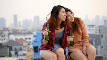 Young woman lesbian couple clinking bottles of beer party on rooftop.