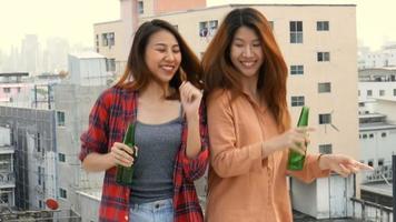 Young woman lesbian couple dancing and clinking bottles of beer party on rooftop. video