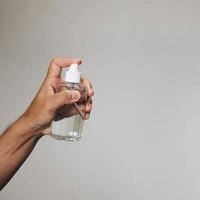 Handsome man holding alcohol spray bottle for hygiene cleaner coronavirus on grey background. photo